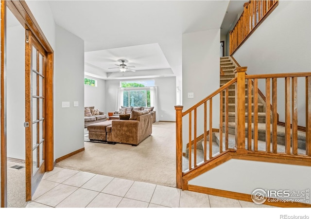 502 Peregrine Cir, Longmont, CO 80504 - living room with light carpet, a ceiling fan, a raised ceiling, stairs, and light tile patterned flooring