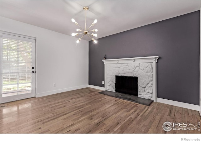 8696 W 86th Cir, Arvada, CO 80005 - unfurnished living room featuring wood finished floors, plenty of natural light, a stone fireplace, and a chandelier