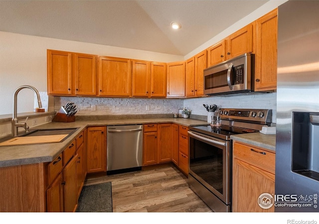 14053 Cottonwood Cir, Sterling, CO 80751 - kitchen with stainless steel appliances, light wood-style flooring, tasteful backsplash, vaulted ceiling, and brown cabinetry