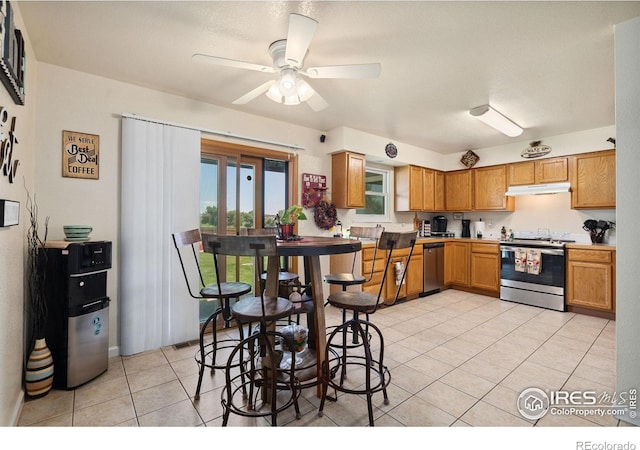 4521 Mesa Verde Dr, Greeley, CO 80634 - kitchen featuring stainless steel appliances, under cabinet range hood, light tile patterned floors, a ceiling fan, and brown cabinets