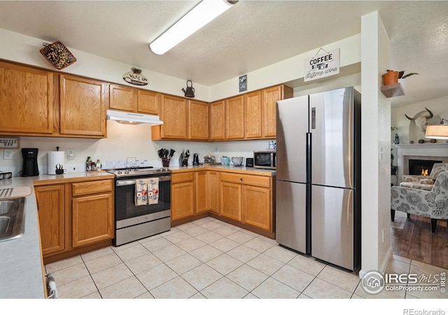 4521 Mesa Verde Dr, Greeley, CO 80634 - kitchen with appliances with stainless steel finishes, under cabinet range hood, light countertops, light tile patterned floors, and a textured ceiling