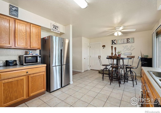 4521 Mesa Verde Dr, Greeley, CO 80634 - kitchen with appliances with stainless steel finishes, a ceiling fan, light tile patterned floors, light countertops, and brown cabinetry