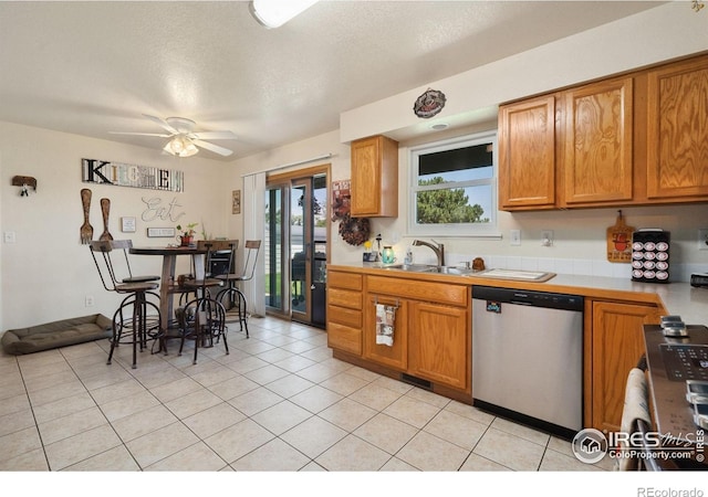 4521 Mesa Verde Dr, Greeley, CO 80634 - kitchen with dishwasher, a ceiling fan, brown cabinetry, light tile patterned floors, and a textured ceiling