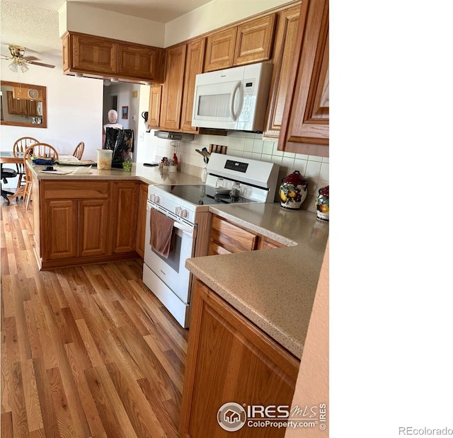 13600 Elmore Rd, Longmont, CO 80504 - kitchen with white appliances, brown cabinets, backsplash, light wood-style floors, and a peninsula