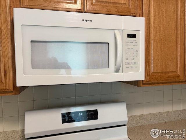 13600 Elmore Rd, Longmont, CO 80504 - detailed view of white microwave, tasteful backsplash, brown cabinetry, and range
