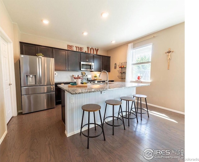 1773 Nightfall Dr, Windsor, CO 80550 - kitchen featuring appliances with stainless steel finishes, dark wood-style floors, a kitchen breakfast bar, an island with sink, and recessed lighting