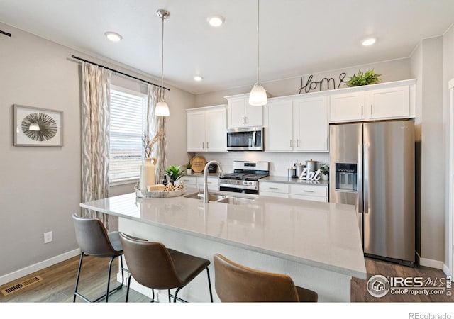 2233 Base St, Fort Lupton, CO 80621 - kitchen with stainless steel appliances, dark wood-style flooring, white cabinetry, a kitchen bar, and recessed lighting