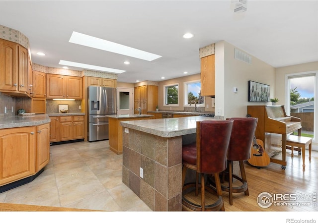 10947 Lynne Ave, Lafayette, CO 80026 - kitchen featuring stainless steel refrigerator with ice dispenser, a skylight, a breakfast bar, backsplash, and a peninsula