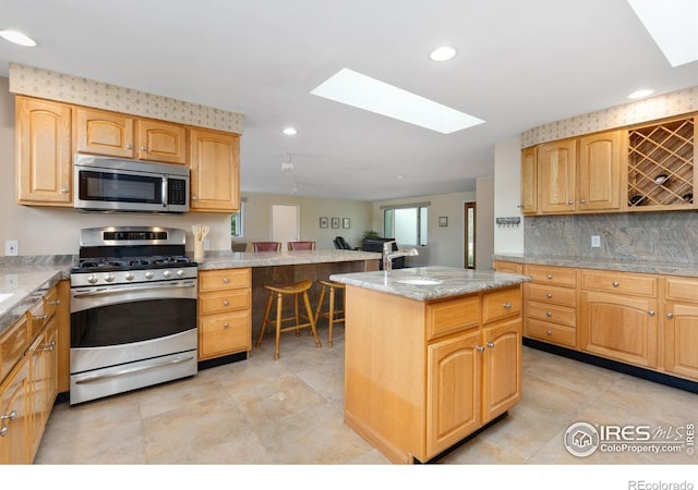 10947 Lynne Ave, Lafayette, CO 80026 - kitchen with stainless steel appliances, a skylight, a kitchen island, decorative backsplash, and light stone countertops