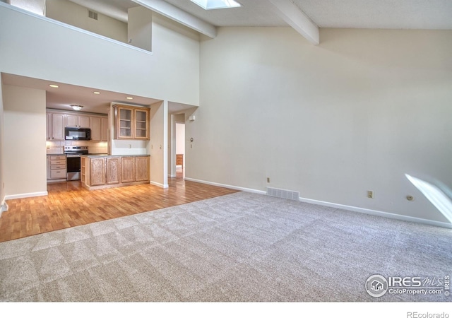 1925 28th Ave Unit 30, Greeley, CO 80634 - unfurnished living room with light carpet, a skylight, beamed ceiling, high vaulted ceiling, and light wood-style floors