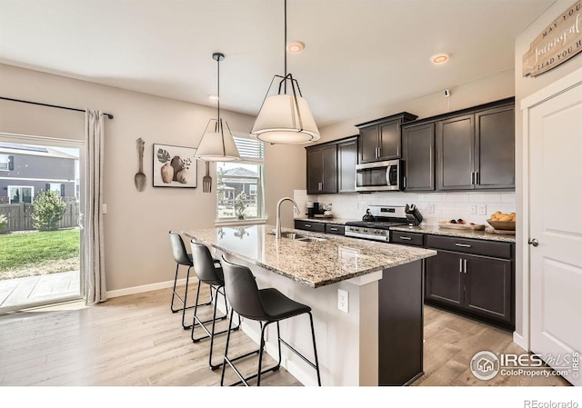 1591 Sun River Rd, Berthoud, CO 80513 - kitchen featuring stainless steel appliances, light wood finished floors, light stone counters, backsplash, and a center island with sink