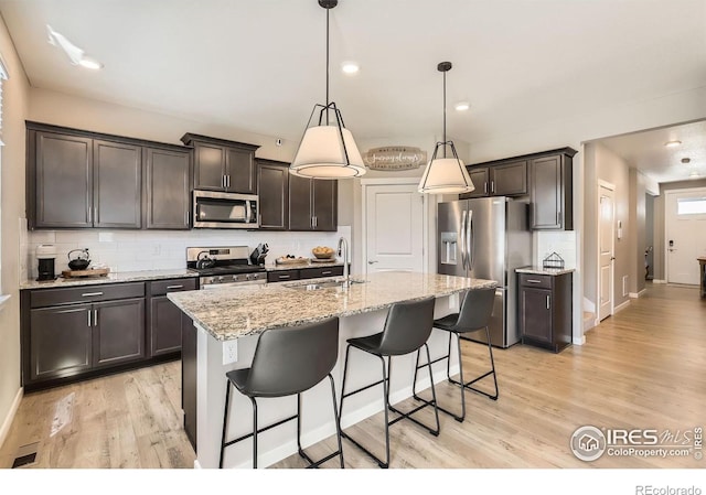 1591 Sun River Rd, Berthoud, CO 80513 - kitchen featuring appliances with stainless steel finishes, tasteful backsplash, light wood finished floors, dark brown cabinets, and light stone countertops