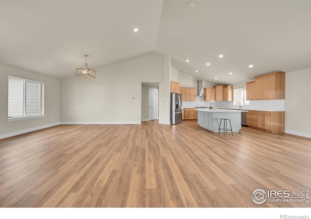 3643 Crested Owl Ct, Dacono, CO 80514 - kitchen featuring appliances with stainless steel finishes, wall chimney exhaust hood, a kitchen bar, light countertops, and open floor plan