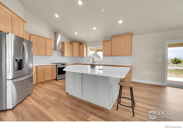 3643 Crested Owl Ct, Dacono, CO 80514 - kitchen with stainless steel appliances, wall chimney exhaust hood, light brown cabinetry, a kitchen island, and lofted ceiling