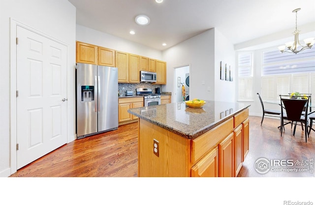 555 S 17th Ave, Brighton, CO 80601 - kitchen featuring stainless steel appliances, a chandelier, wood finished floors, a kitchen island, and decorative backsplash