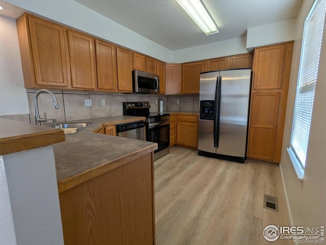 3705 Dove Ln, Evans, CO 80620 - kitchen featuring appliances with stainless steel finishes, light wood finished floors, backsplash, a peninsula, and plenty of natural light