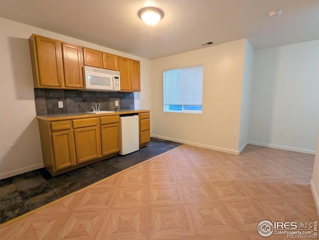 3705 Dove Ln, Evans, CO 80620 - kitchen featuring white appliances, decorative backsplash, brown cabinets, and a textured ceiling