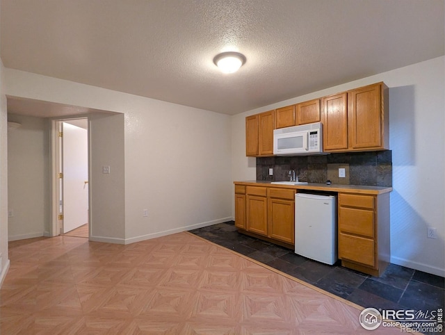 3705 Dove Ln, Evans, CO 80620 - kitchen featuring white appliances, a textured ceiling, tasteful backsplash, and brown cabinetry