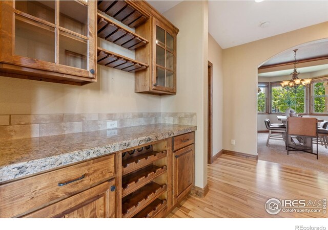 8276 Blackwood Dr, Windsor, CO 80550 - kitchen with brown cabinets, light wood finished floors, a chandelier, and arched walkways