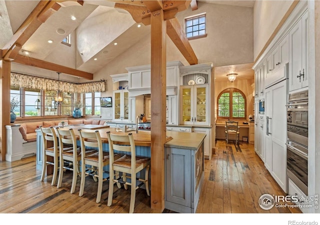 6619 Ridgeline Dr, Timnath, CO 80547 - kitchen with high vaulted ceiling, light wood-type flooring, white cabinetry, beamed ceiling, and glass insert cabinets