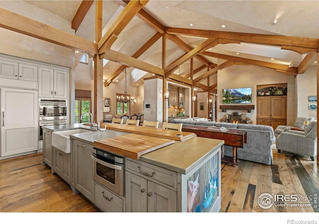 6619 Ridgeline Dr, Timnath, CO 80547 - kitchen featuring open floor plan, beamed ceiling, a chandelier, a center island with sink, and hardwood / wood-style flooring