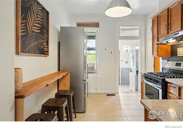 2955 Columbine St, Denver, CO 80205 - kitchen with under cabinet range hood, stainless steel appliances, brown cabinetry, light tile patterned flooring, and crown molding