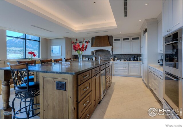 1077 Canyon Blvd # 403, Boulder, CO 80302 - kitchen featuring premium range hood, double oven, a breakfast bar, decorative backsplash, and a tray ceiling