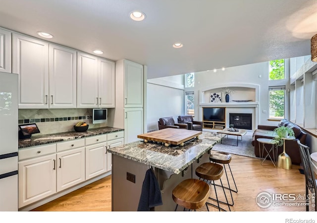 6366 Umber Cir, Arvada, CO 80403 - kitchen featuring a kitchen breakfast bar, light wood finished floors, dark stone counters, white cabinetry, and recessed lighting