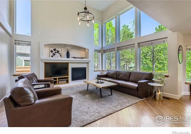 6366 Umber Cir, Arvada, CO 80403 - living room featuring a towering ceiling, hardwood / wood-style floors, a chandelier, and a glass covered fireplace