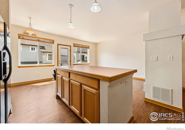 3686 Oakwood Dr, Longmont, CO 80503 - kitchen with a kitchen island, wood finished floors, refrigerator with ice dispenser, hanging light fixtures, and light countertops
