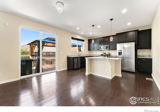 5049 S Ukraine St, Aurora, CO 80015 - kitchen featuring stainless steel appliances, a kitchen island, light stone countertops, dark wood-style floors, and recessed lighting