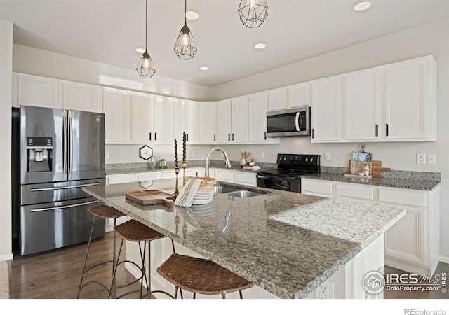 5217 Alberta Falls St, Timnath, CO 80547 - kitchen featuring appliances with stainless steel finishes, white cabinetry, light stone counters, hanging light fixtures, and a kitchen island with sink