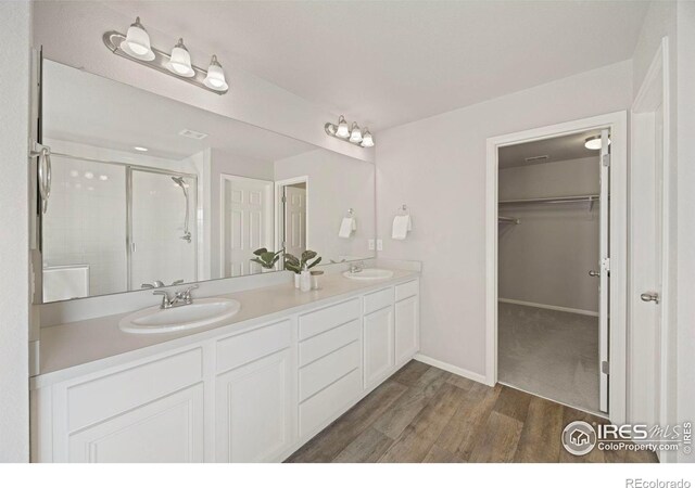 5217 Alberta Falls St, Timnath, CO 80547 - bathroom featuring a stall shower, double vanity, a walk in closet, and wood finished floors