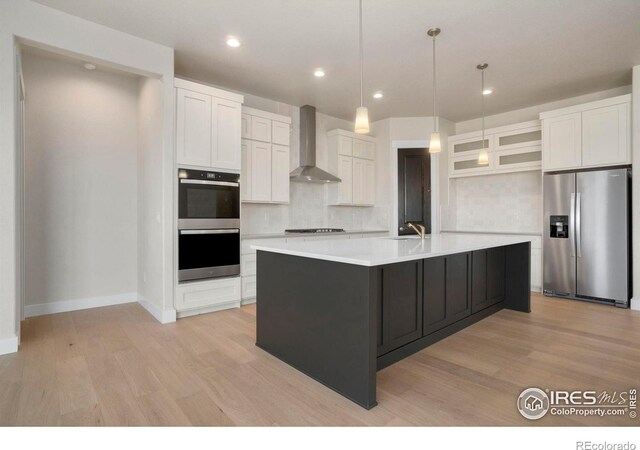 24113 E 36th Pl, Aurora, CO 80019 - kitchen with appliances with stainless steel finishes, wall chimney exhaust hood, light wood-style floors, tasteful backsplash, and white cabinets