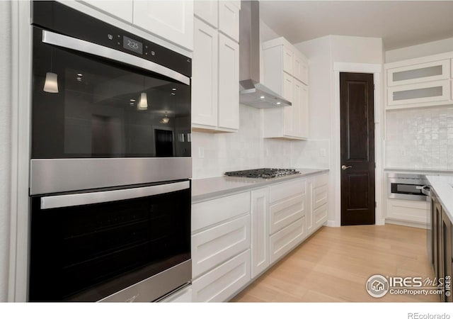 24113 E 36th Pl, Aurora, CO 80019 - kitchen with appliances with stainless steel finishes, wall chimney exhaust hood, white cabinetry, backsplash, and light wood finished floors