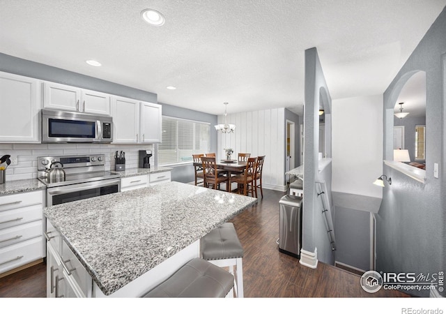 2302 74th Ave, Greeley, CO 80634 - kitchen featuring stainless steel microwave, white cabinetry, dark wood finished floors, a textured ceiling, and light stone countertops