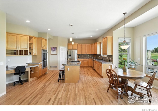 1145 Wyndemere Cir, Longmont, CO 80504 - kitchen featuring open shelves, stainless steel appliances, built in study area, a kitchen bar, and light wood finished floors
