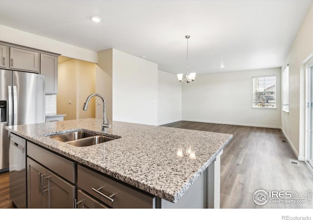9929 Ceylon Ct, Commerce City, CO 80022 - kitchen featuring stainless steel appliances, gray cabinetry, wood finished floors, a center island with sink, and light stone counters