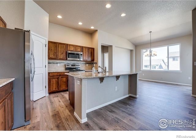 604 Rosedale St, Severance, CO 80550 - kitchen featuring stainless steel appliances, brown cabinetry, wood finished floors, a chandelier, and a breakfast bar