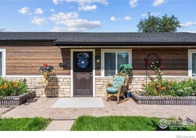 7131 Pontiac St, Commerce City, CO 80022 - doorway to property featuring stone siding, a shingled roof, and covered porch