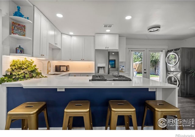 7131 Pontiac St, Commerce City, CO 80022 - kitchen featuring stacked washing machine and dryer, appliances with stainless steel finishes, a peninsula, white cabinetry, and recessed lighting