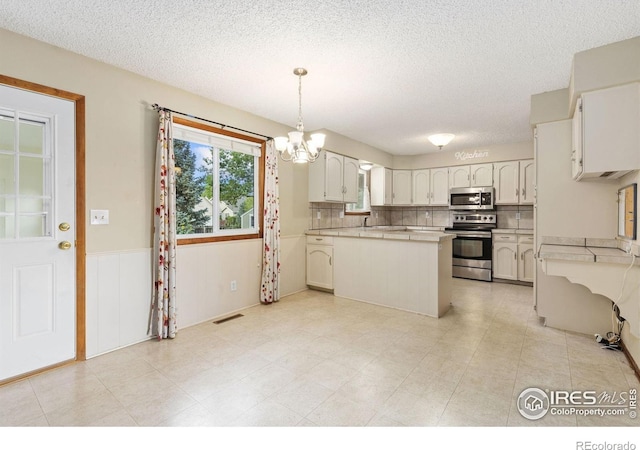 2516 Mountain View Ave, Longmont, CO 80503 - kitchen with appliances with stainless steel finishes, a textured ceiling, light countertops, a chandelier, and wainscoting