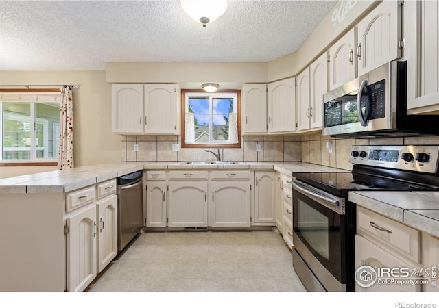 2516 Mountain View Ave, Longmont, CO 80503 - kitchen featuring appliances with stainless steel finishes, a peninsula, backsplash, a textured ceiling, and healthy amount of natural light