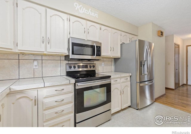 2516 Mountain View Ave, Longmont, CO 80503 - kitchen with stainless steel appliances, tile counters, tasteful backsplash, light tile patterned floors, and a textured ceiling