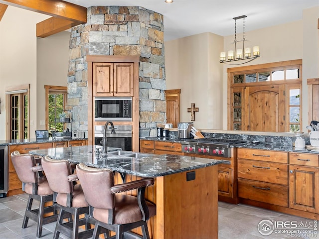 3411 Hillcrest Ln, Estes Park, CO 80517 - kitchen with stainless steel appliances, brown cabinetry, dark stone countertops, an island with sink, and beverage cooler