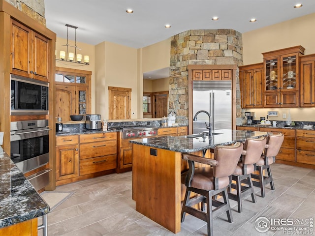3411 Hillcrest Ln, Estes Park, CO 80517 - kitchen with built in appliances, brown cabinetry, a breakfast bar, a center island with sink, and dark stone counters
