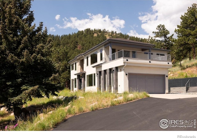 514 Granite Dr, Boulder, CO 80302 - view of front of property with a balcony, driveway, stucco siding, an attached garage, and a forest view
