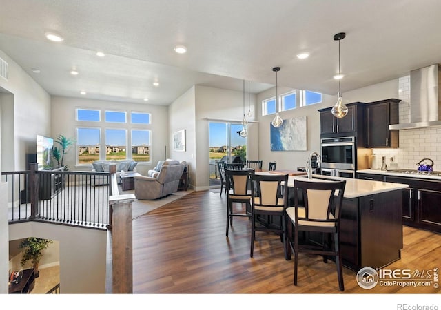2772 Vallecito St, Timnath, CO 80547 - kitchen with wall chimney exhaust hood, wood finished floors, a kitchen island with sink, light countertops, and a breakfast bar area