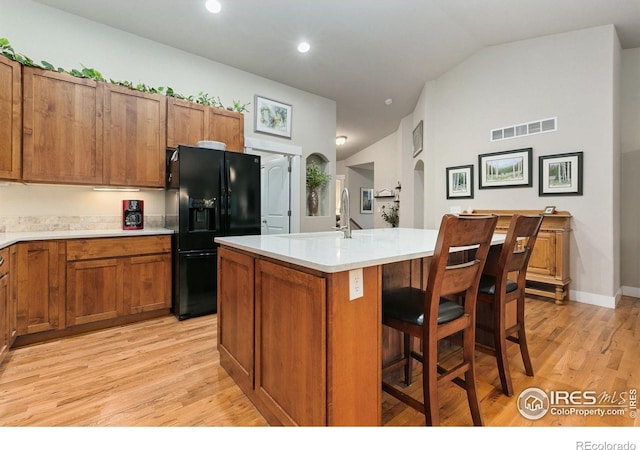 83 Evans St, Severance, CO 80550 - kitchen featuring black fridge with ice dispenser, brown cabinets, light wood finished floors, a kitchen island with sink, and light countertops