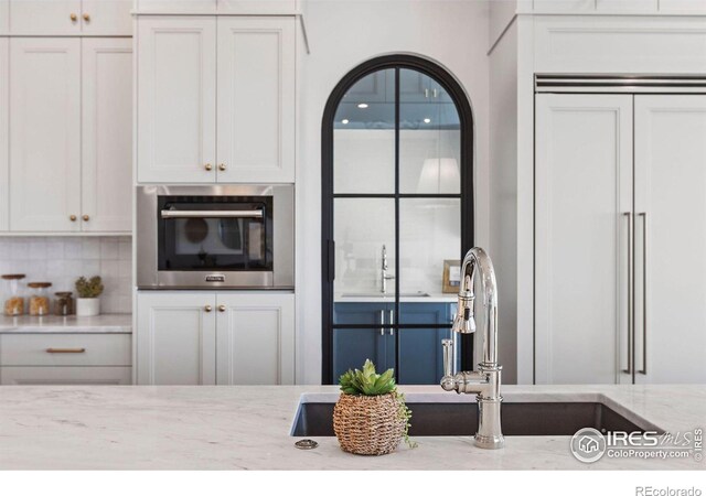 2568 Southwind Rd, Berthoud, CO 80513 - kitchen featuring oven, light stone countertops, backsplash, white cabinets, and paneled built in refrigerator